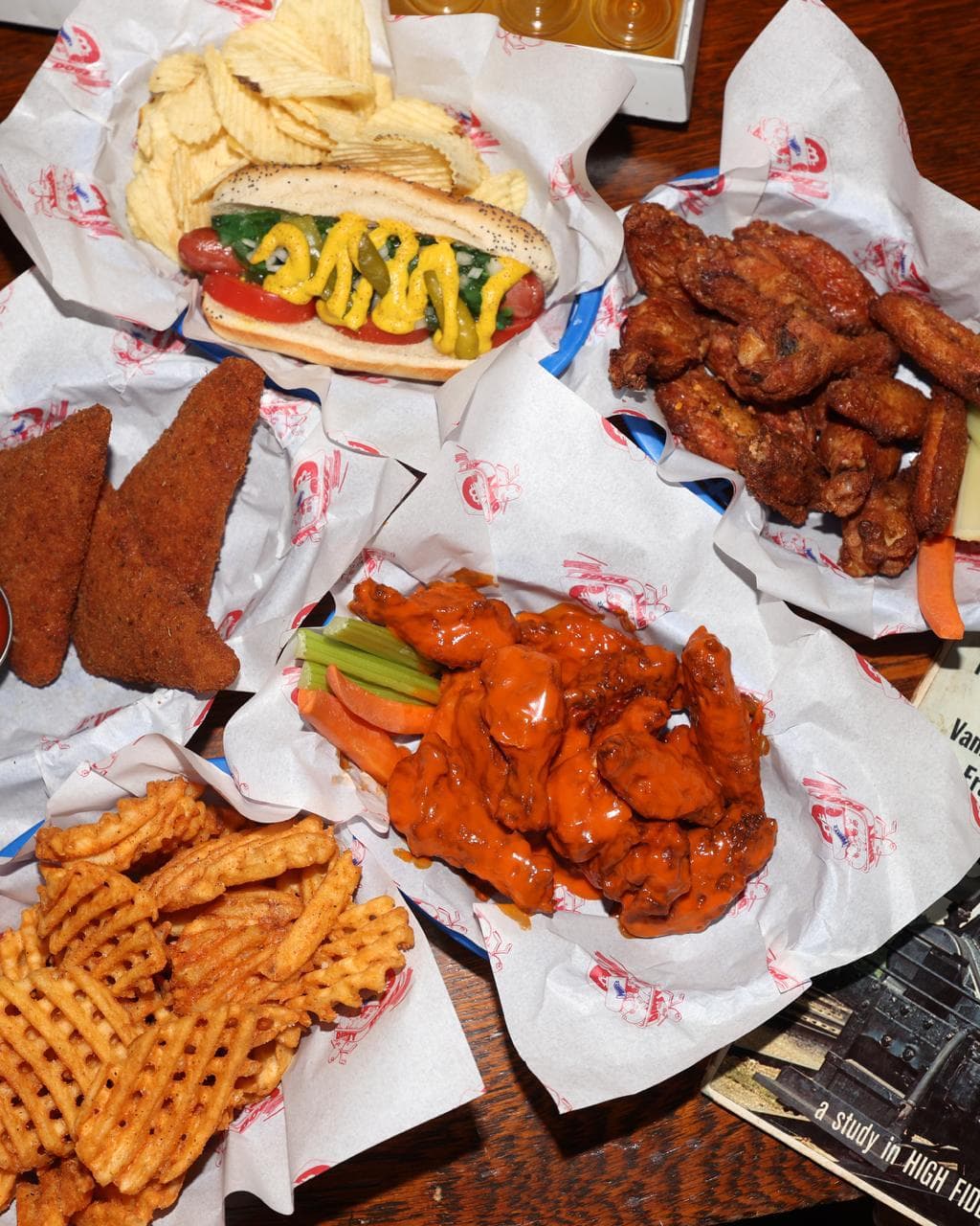 A table of baskets at PubKey: a Chicago-style hot dog with chips, wings, waffle fries, and buffalo tenders