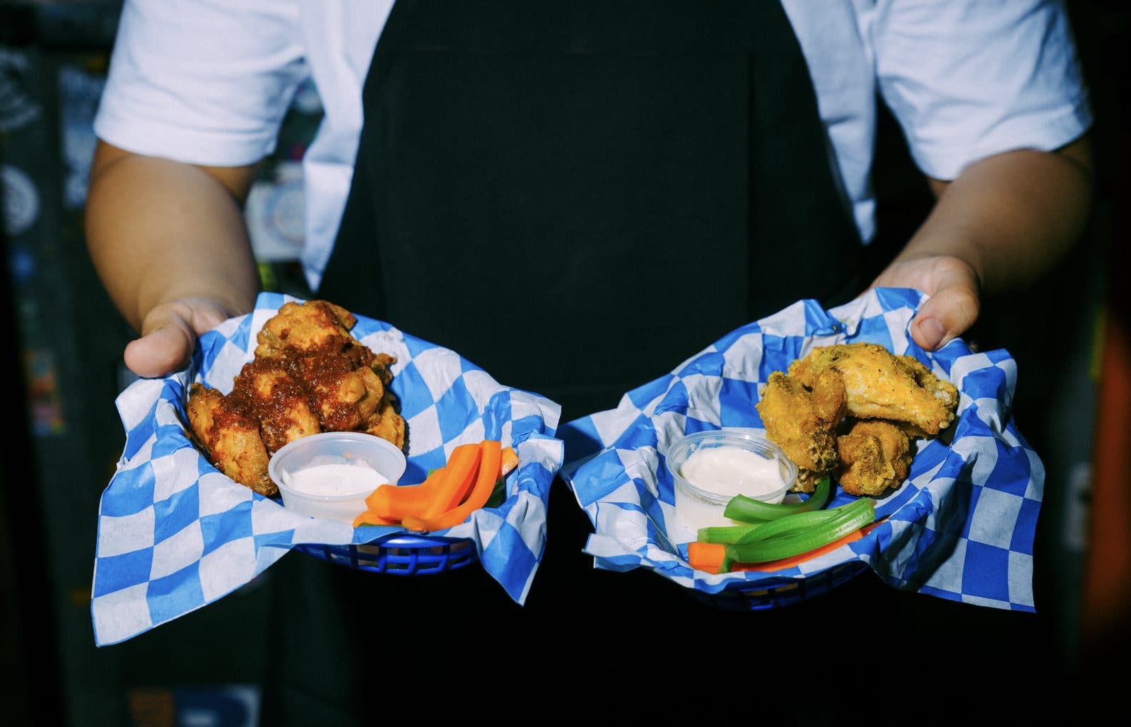 A server holding out two baskets of wings with ranch and celery